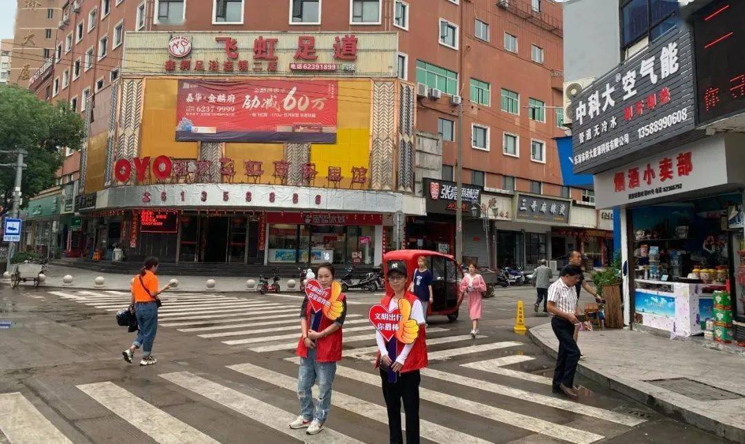 者在进行交通秩序劝导工作,路口边的行人和车辆正耐心的等待着红灯