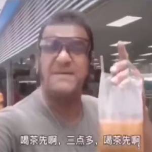 下戴着褐色墨镜,用食指顶着袋装奶茶,对着手机镜头大喊"饮茶先"的男人