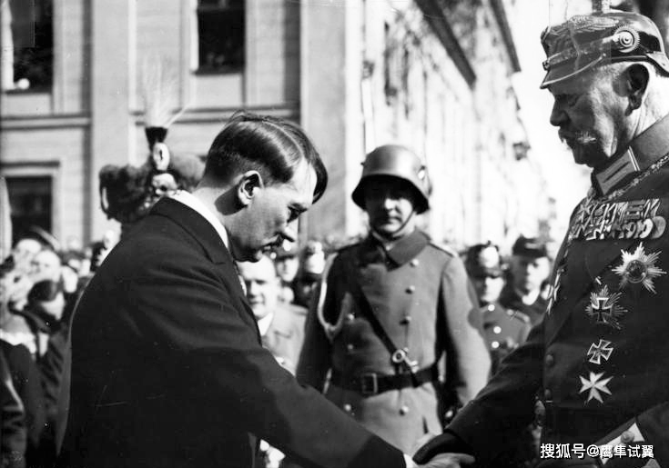 图中草根传奇希特勒在和军事贵族兴登堡握手,希特勒低头,表现出一副