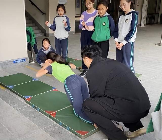 小学内,教学楼楼梯口的过道中,有一群穿着校服的小学女生正在上体育课