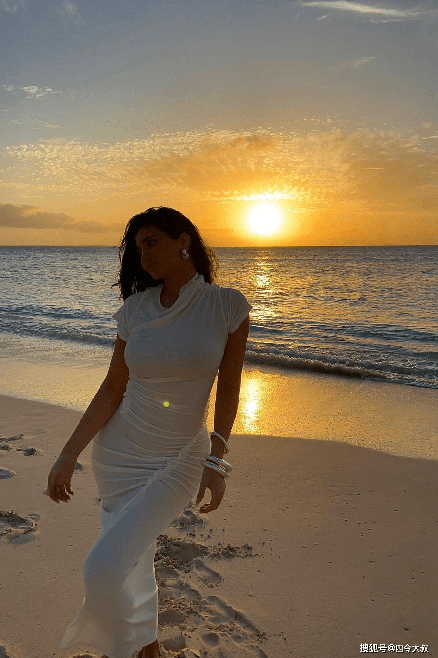 凯莉·詹娜身穿白色紧身落地长裙,长长的波浪形棕色头发飘在身后,画面