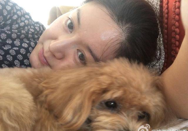 照片中柏雪妆容清淡打扮朴素,身穿灰色毛衣的她坐在沙发上,还抱着一只