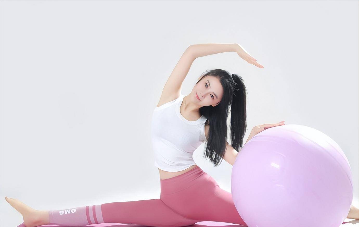 她留着长发,戴着围巾,杏颊,红唇,洁白的牙齿;她在瑜伽垫上做小马,动作