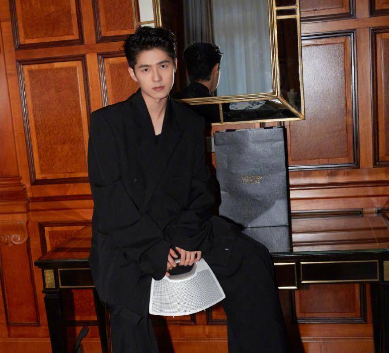 时装秀上,刘昊然身穿西装外套和西装裤,手上拎着一个白色的包包.