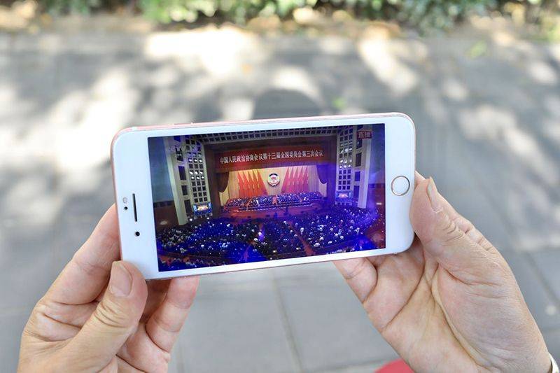 一名值勤的志愿者通过手机观看全国政协十三届三次会议闭幕会直播