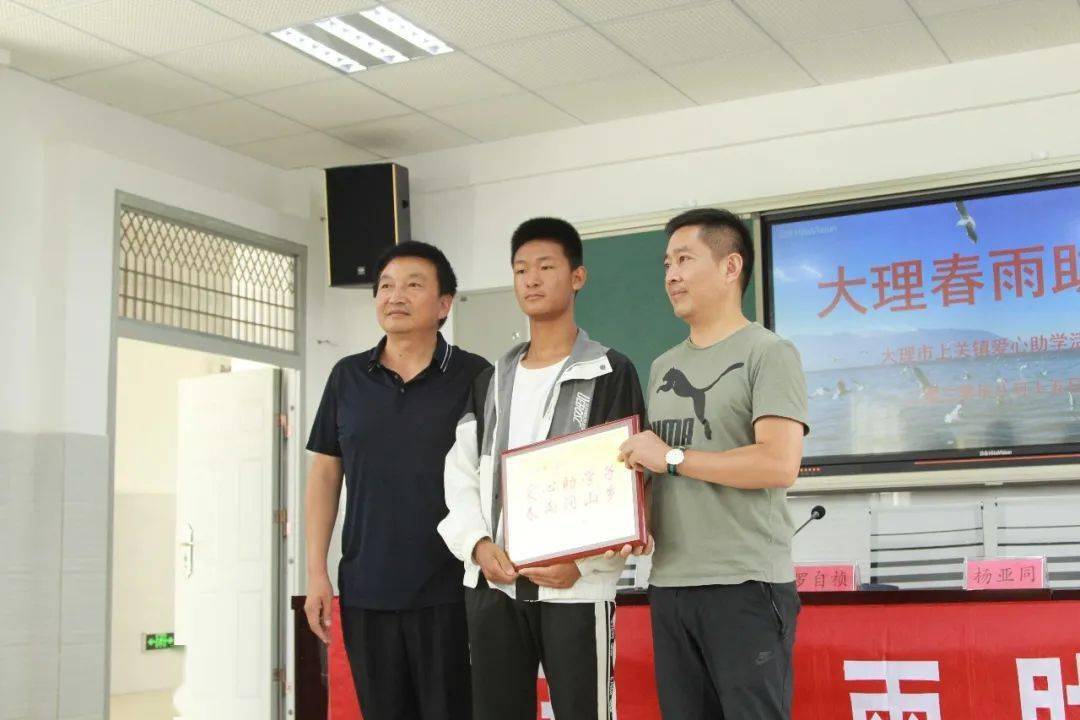大理市上关镇第二初级中学校长王洪泽(左)为陈尚炜爱心家庭颁授爱心