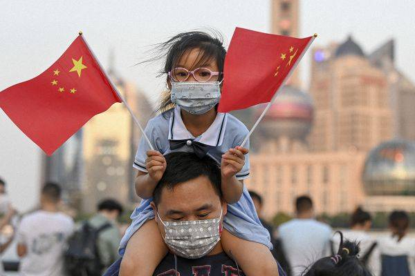 一位小女孩拿着五星红旗,坐在家长肩膀上.