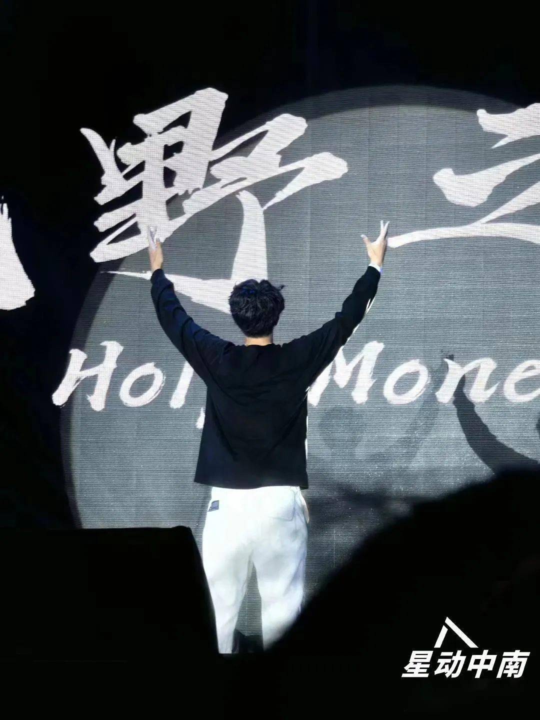舞台的ending pose万大千背对舞台手拿话筒高举双臂无数光点组成的